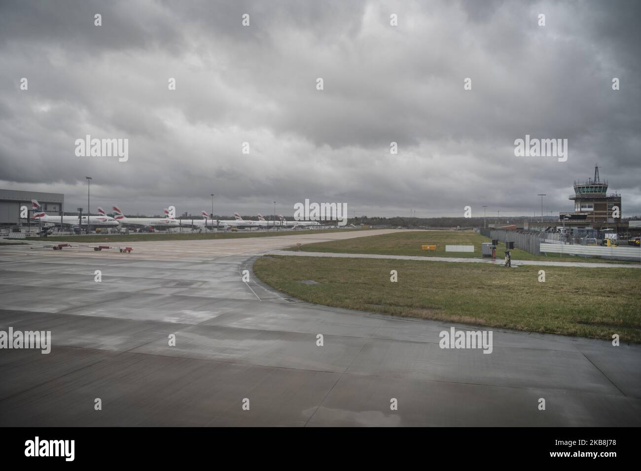 Flugzeuge am Flughafen Gatwick parkten im Hintergrund Frachtschuppen mit Flugsicherungsturm-Rollbahn bewölktem Wintertag Stockfoto