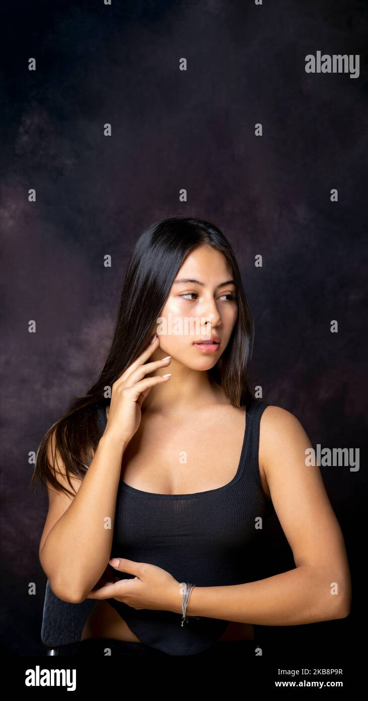 Multirassische Teen mit langen schönen Haaren sitzend mit Armen in Tanzpose mit Blick weg von der Kamera mit Copy Space über ihr Stockfoto