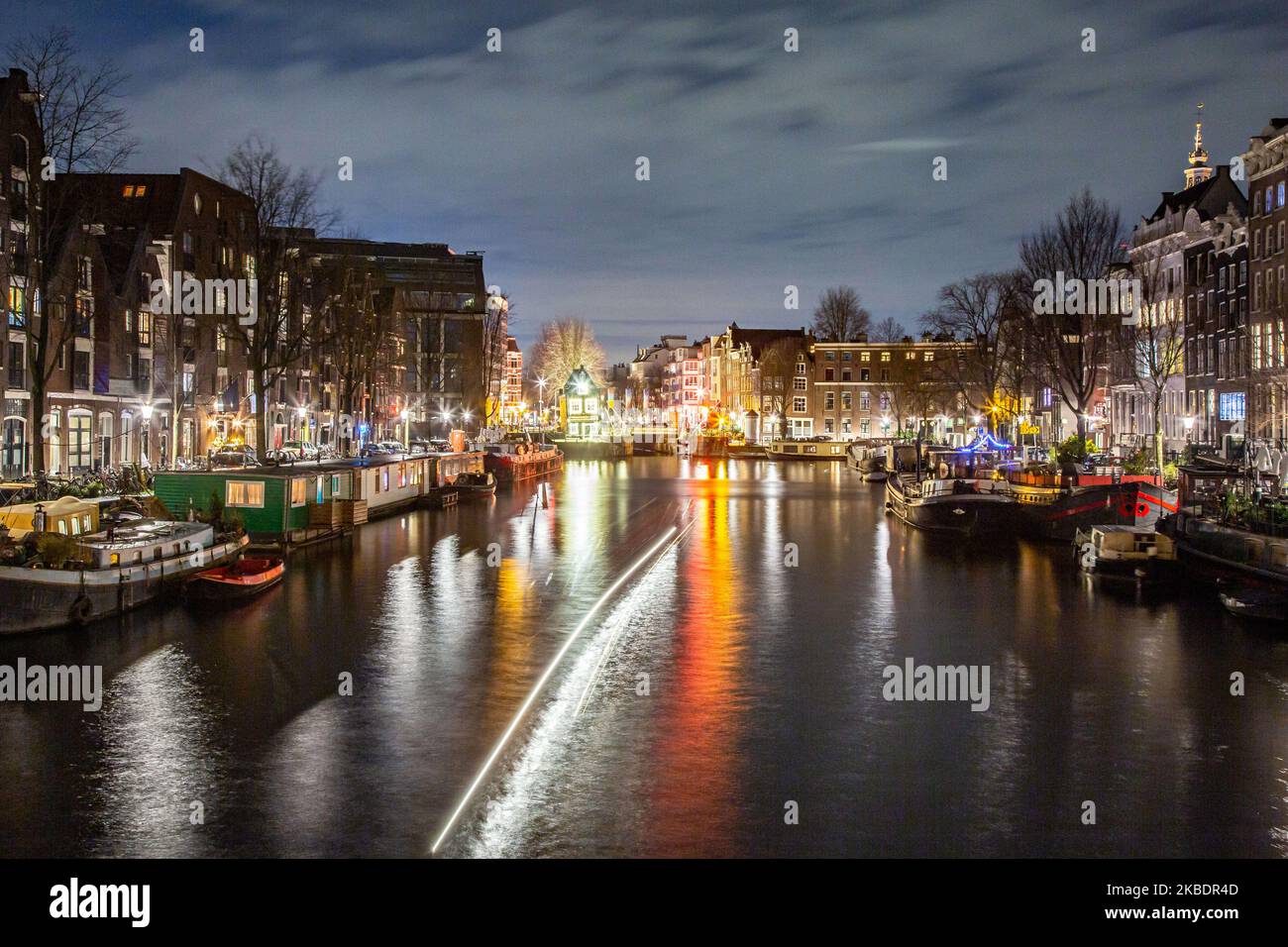 Grachten in Amsterdam wie Amstel mit typischen traditionellen alten niederländischen Architektur Häuser beleuchtet und Hausboote am Abend und Nacht mit schönen Wasserspiegelungen und Stadtlichter, Holland, Niederlande. Amsterdam ist ein Finanzzentrum, aber auch eine der meistbesuchten Städte Europas, die Millionen von Touristen auf der ganzen Welt anzieht, wobei der Tourismus eine wichtige Rolle in der lokalen Wirtschaft spielt, obwohl es Stimmen gegen diese touristische Entwicklung gibt. (Foto von Nicolas Economou/NurPhoto) Stockfoto