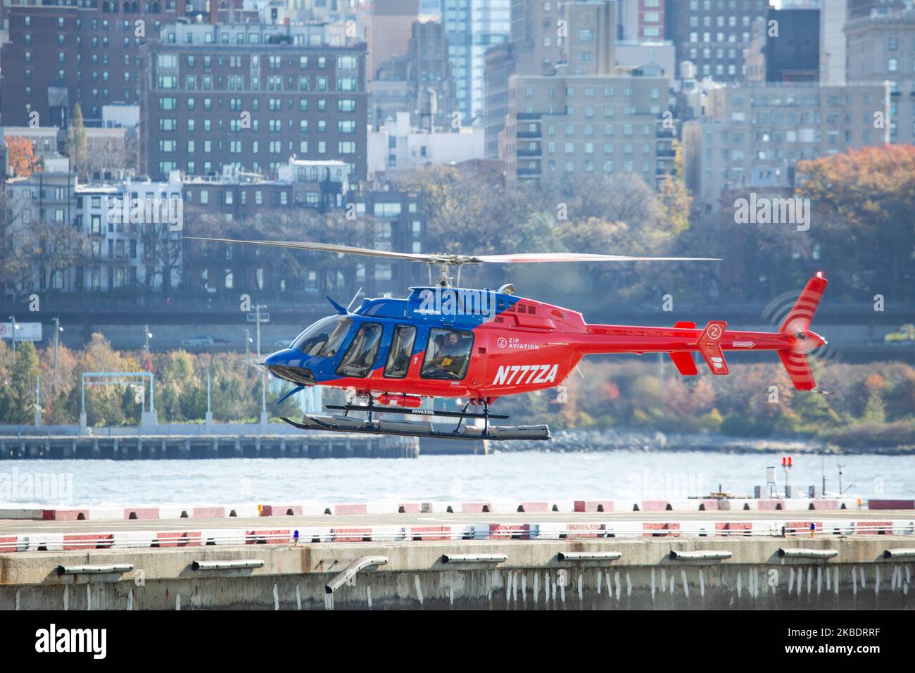 Ein rot-blauer Helikopter Bell 407GXP mit der Registrierung N777ZA von Zip Aviation voller Passagiere, wie man sieht, dass er auf dem Hubschrauberlandeplatz der New York Port Authority Downtown Manhattan Wall Street JRB KJRB Heliport-Plattform am Pier 6 im East River, Lower Manhattan in New York City landet, USA mit dem Fluss und den Gebäuden von Brooklyn im Hintergrund. Es ist eine beliebte Attraktion für Touristen, da sie mit den Sightseeing-Hubschrauberflügen eine Panoramaansicht von NYC erhalten. (Foto von Nicolas Economou/NurPhoto) Stockfoto