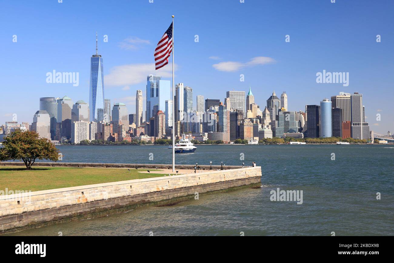 Panoramablick auf die Wolkenkratzer von New York City (Lower Manhattan) von Ellis Island mit amerikanischer Flagge im Vordergrund, USA Stockfoto