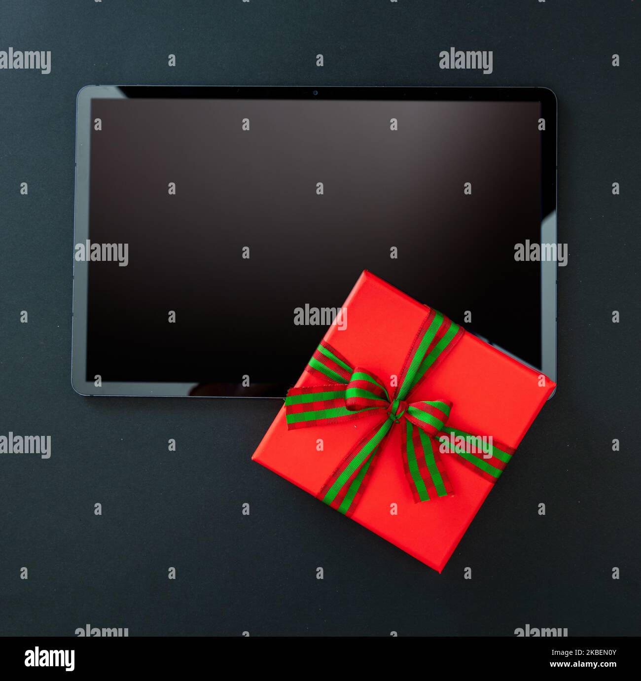 Cyber Monday und Black Friday Sale. Rote Geschenkbox mit Schleife auf digitalem Tablet, schwarzer Hintergrund, Draufsicht Stockfoto