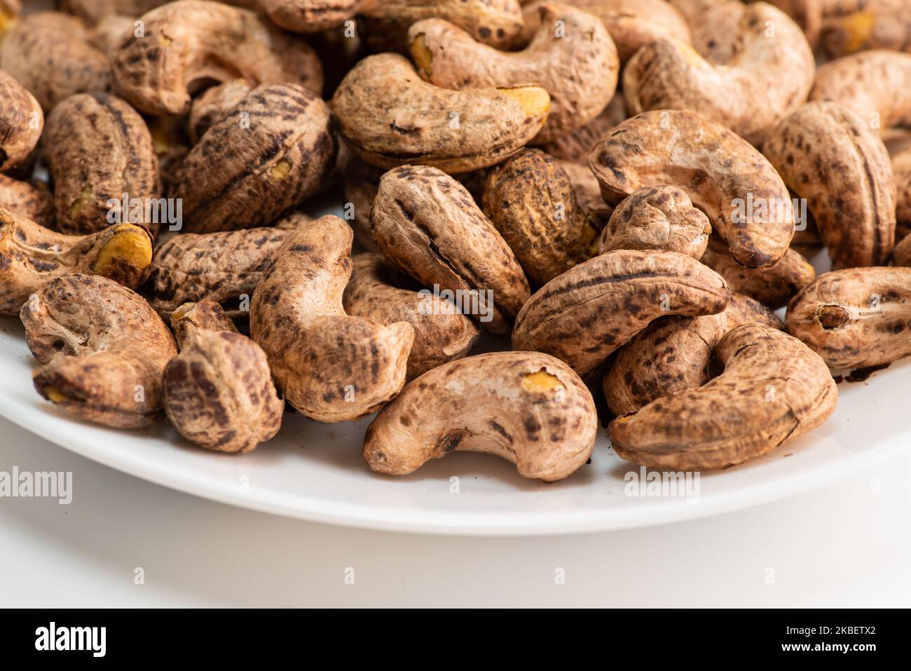 Nahaufnahme von gerösteten Cashewnüssen mit Haut auf weißem Hintergrund Stockfoto