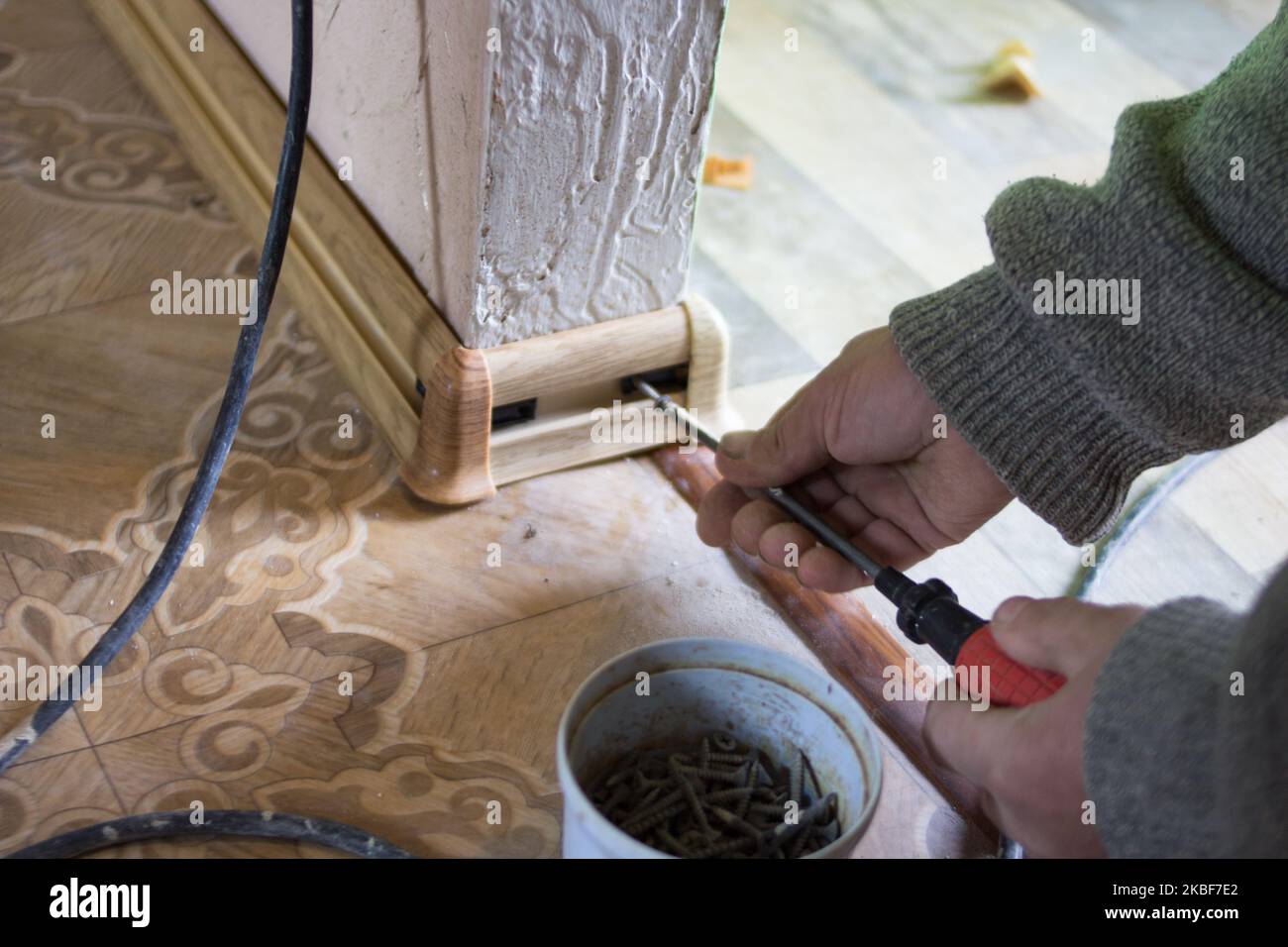 Mann dreht die Sockelleiste mit einem Schraubendreher auf dem Boden Stockfoto