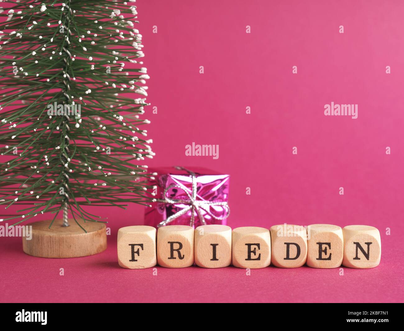 Kleine Holzblöcke mit der deutschen Aufschrift Peace, Merry Christmas, lila Hintergrund, minimalistische Holzweihnachtsdekoration Stockfoto