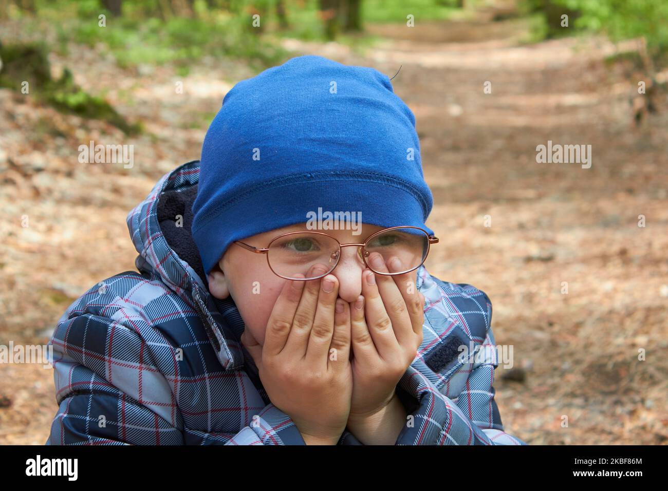 Junge in einer Brille bedeckt sein Gesicht im Herbst mit den Händen Stockfoto