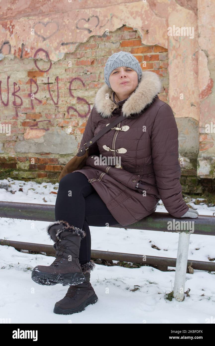 Das Mädchen saß im Winter auf der alten Straße auf dem Metallgeländer Stockfoto