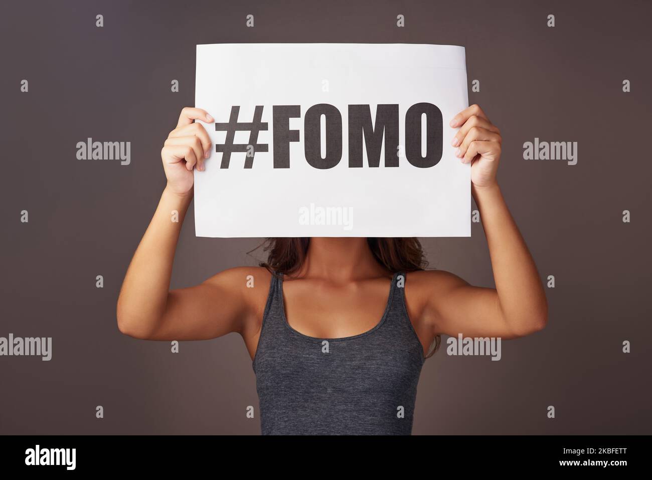 Aus den Augen, nie aus dem Kopf. Studioaufnahme einer jungen Frau mit einem Schild, auf dem FOMO vor grauem Hintergrund gedruckt ist. Stockfoto