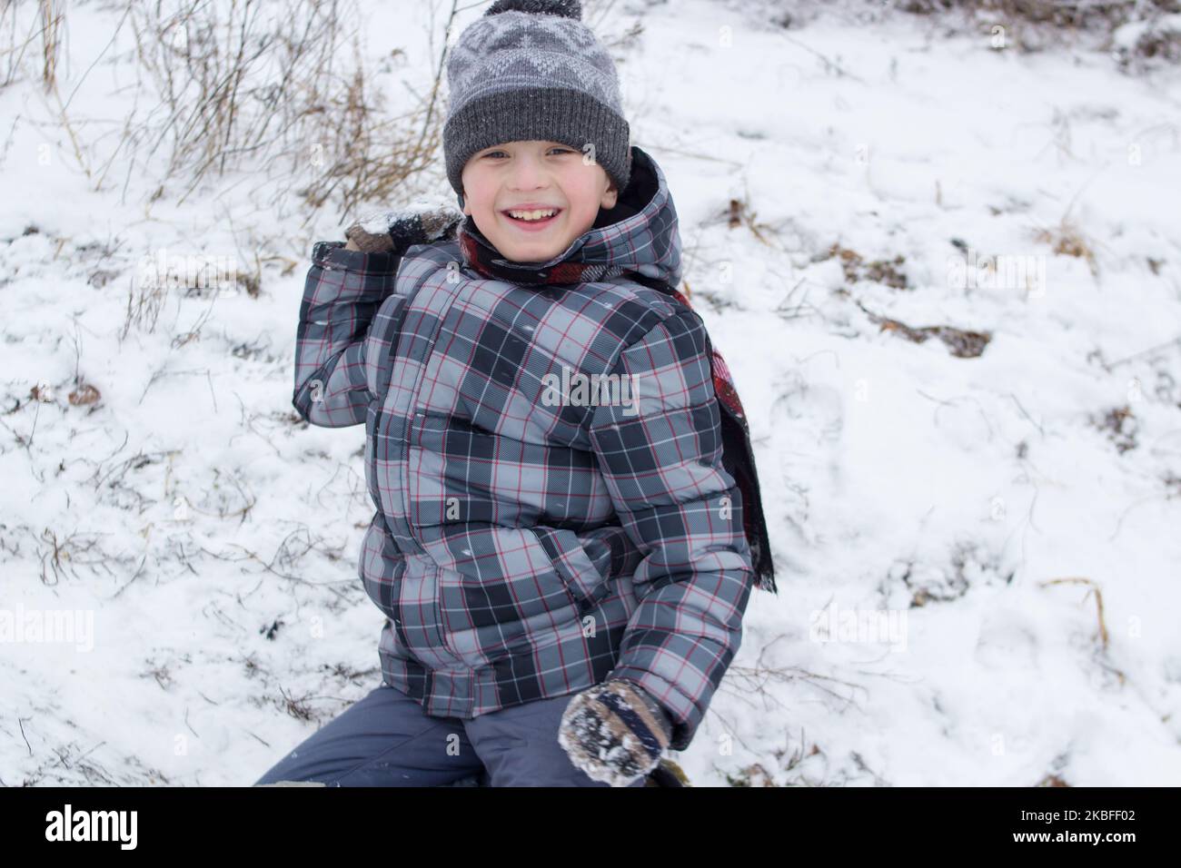 Der Junge lacht und wirft Schneebälle im Winter Stockfoto