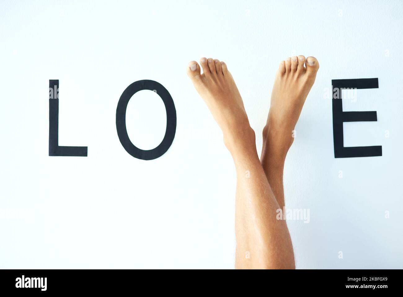 Wandelt auf dem Pfad der Liebe. Studioaufnahme eines nicht erkennbaren mannes kreuzte die Beine, wobei seine Füße den Buchstaben V im Wort LIEBE bildeten. Stockfoto