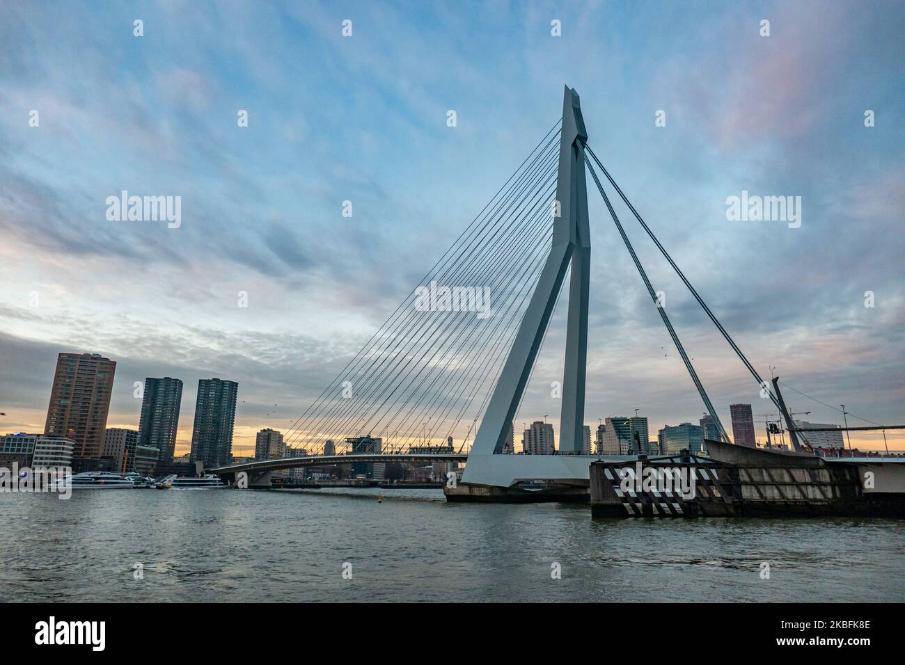 Erasmusbrug oder die Erasmus-Brücke, wie sie am 20. Januar 2020 in einer magischen Stunde am Winterabend mit buntem Himmel im Stadtzentrum der niederländischen Stadt Rotterdam, Niederlande, zu sehen ist. Die 802m. Lange Brücke über das Wasser der Neuen Maas ist eine von Ben van Berkel entworfene, nach Desiderius Erasmus benannte Brücke mit Kabelgestellen und Bascule. Die Konstruktion und die Struktur sind berühmt für ihre moderne Architektur und das asymmetrische, blassblaue Pylondesign, das auch die größte Platte seiner Art in der Welt hat. Die Brücke ist ein Wahrzeichen, Denkmal für Rotterdam und die Niederlande. (Foto von Nicolas Economou/NurP Stockfoto