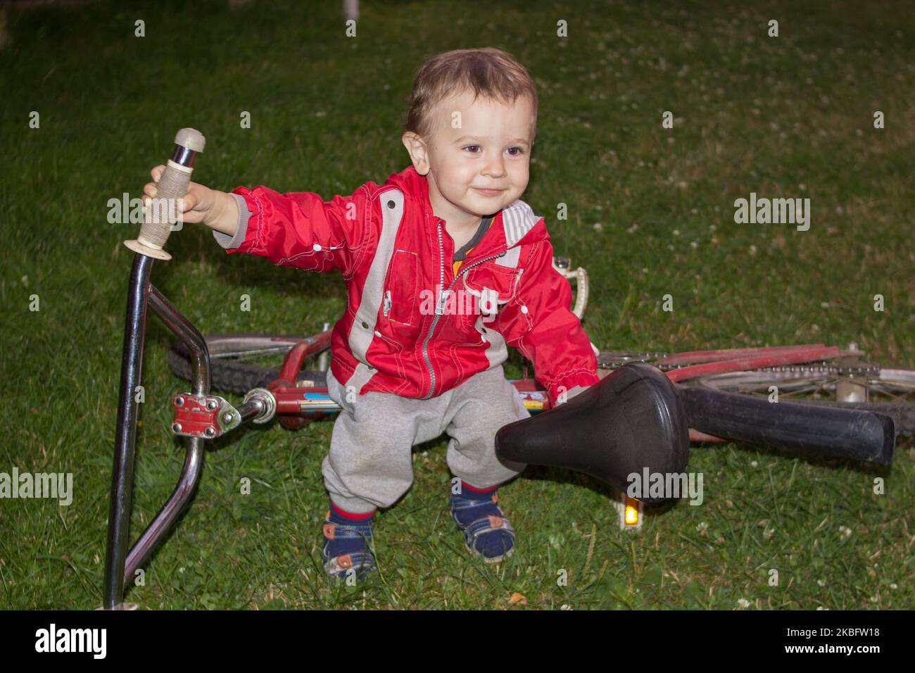 Nachts sitzt ein kleiner Junge auf einem Fahrrad, das auf dem Gras liegt Stockfoto