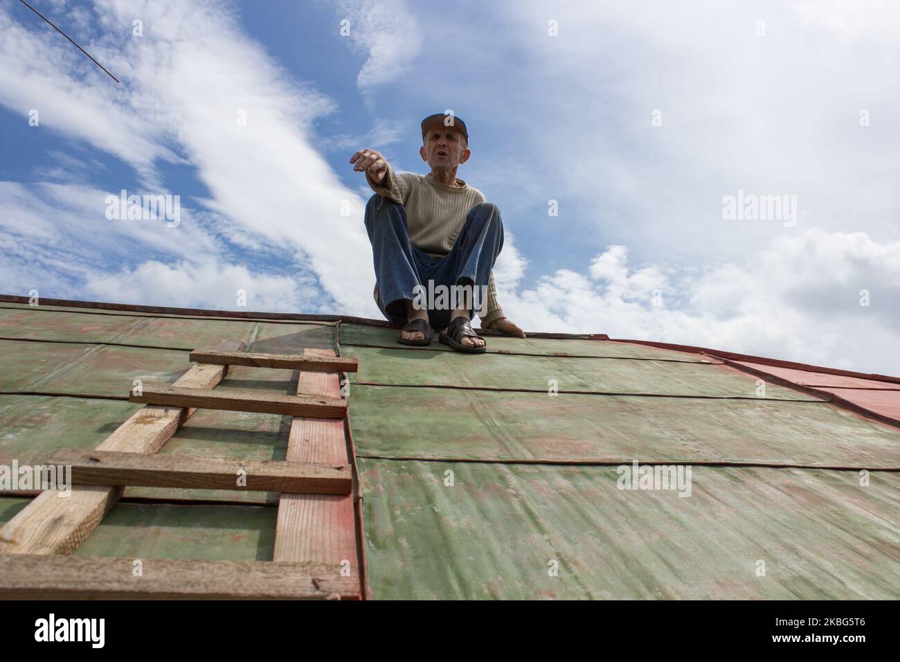 Älterer Mann, der auf dem Dach des Hauses sitzt und seine Hände zeigt Stockfoto