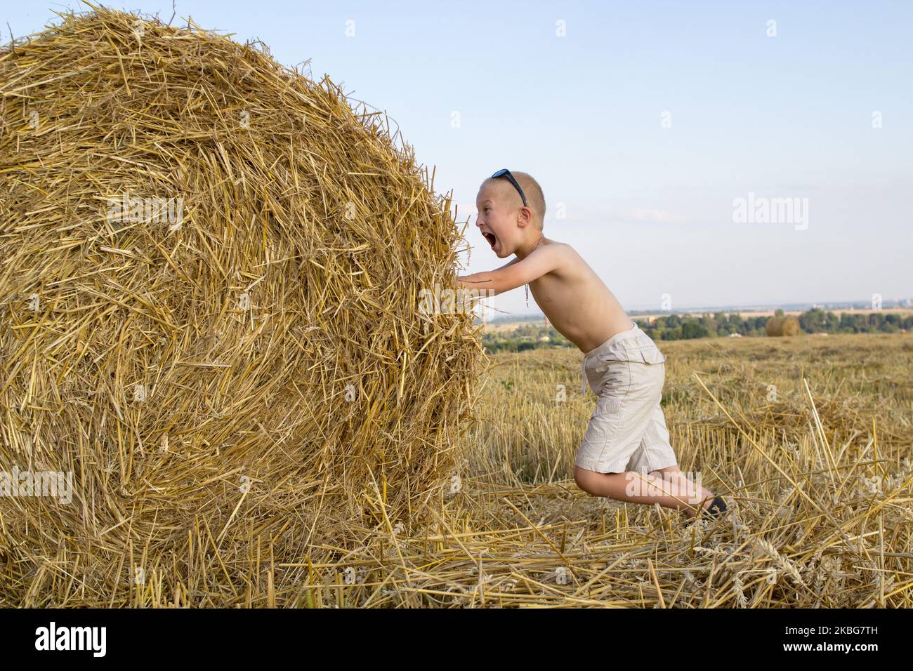 Ein Junge auf dem Feld mit einem Schrei schiebt einen Heuballen Stockfoto