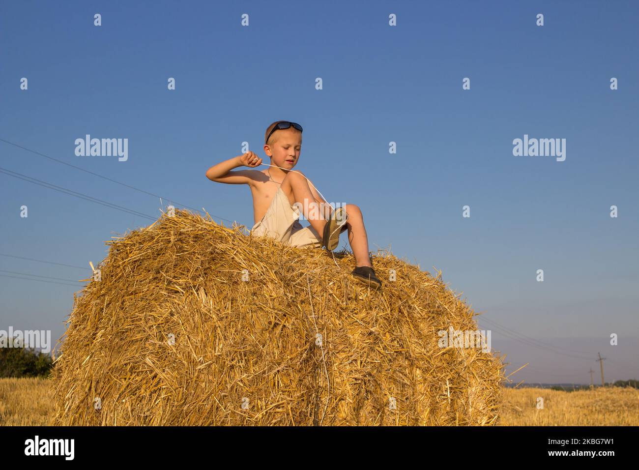 Bei Sonnenuntergang sitzt der Junge auf dem Feld für einen Strohballen Stockfoto