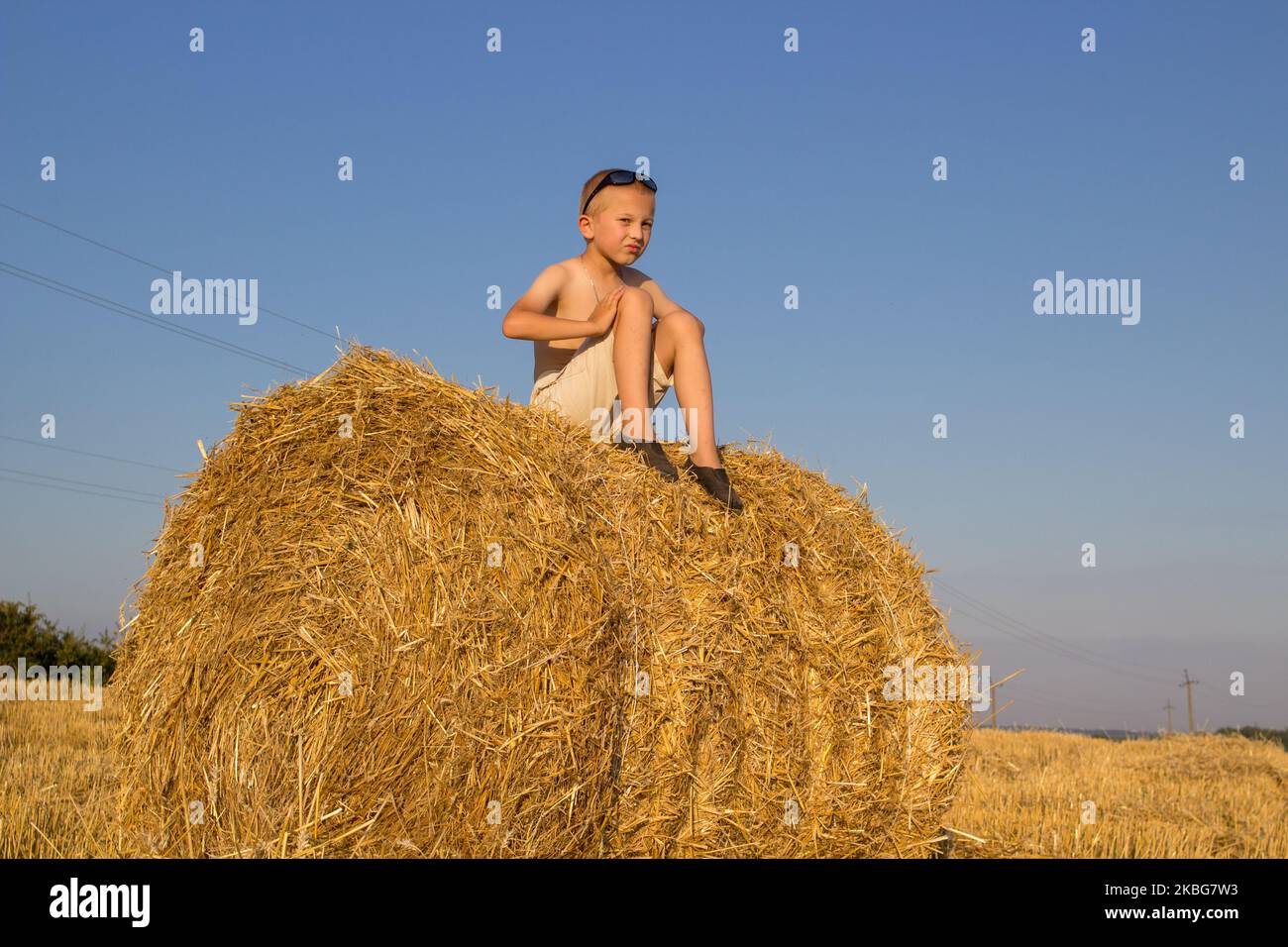 Heuhaufen sitzender Junge, kleine nette Jungen Shorts und modern sitzt auf einem Heuhaufen an einem Sommertag. Ernte. Stockfoto