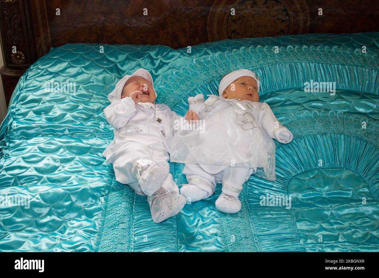 Kleine Mädchen- und Jungzwillinge sind auf dem großen Bett in Weiß gekleidet Stockfoto