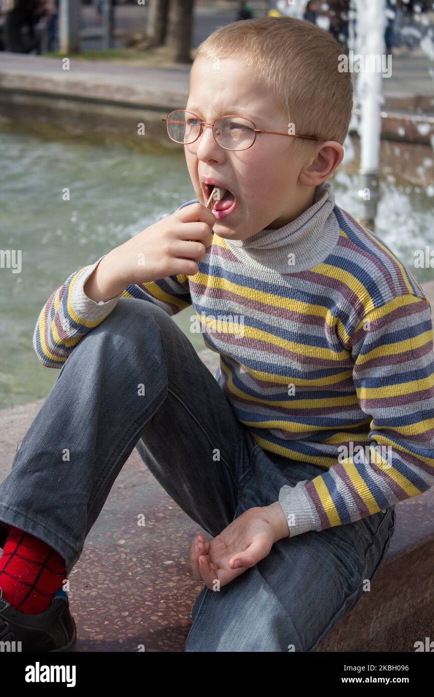 Lustiger Junge in Gläsern mit offenem Mund, der Eis isst Stockfoto
