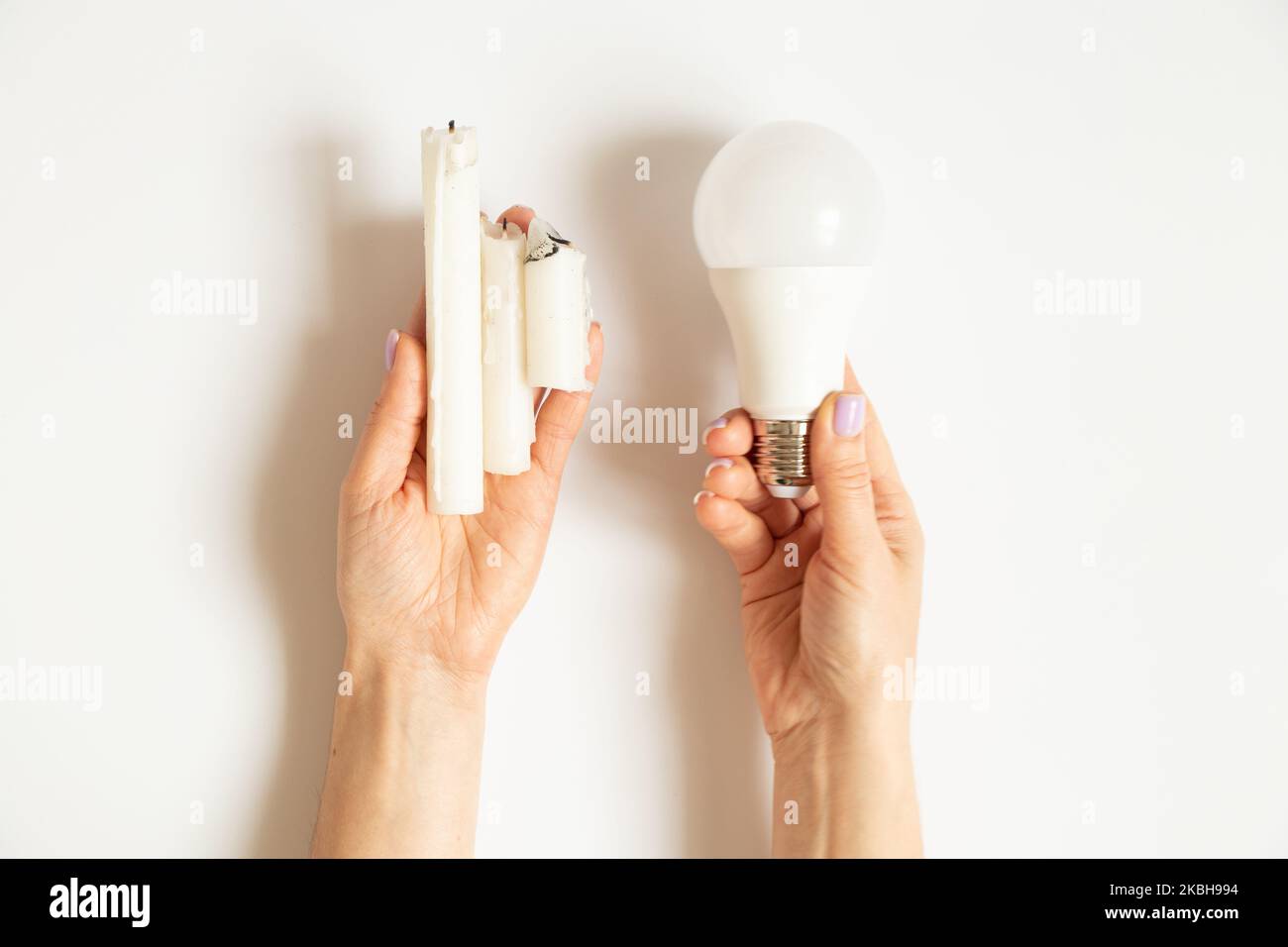 LED-Glühbirne und Kerzen in den Händen eines Mädchens auf weißem Hintergrund, Strom- und Sparmöglichkeit, kein Licht Stockfoto
