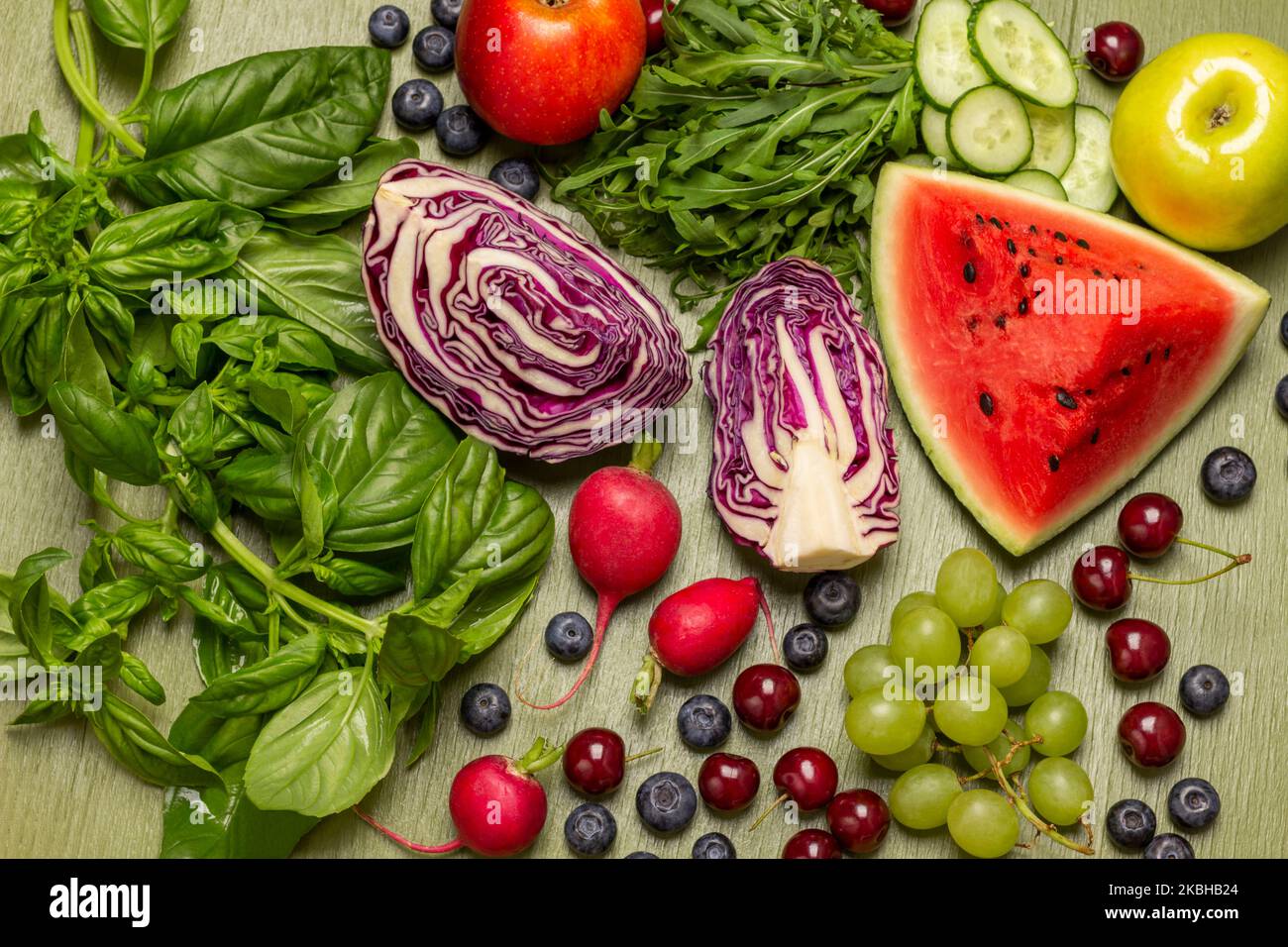 Mischung aus frischem Gemüse, Obst, Beeren und Gemüse. Zweige aus grünem Basilikum und Rucola. Flach liegend. Grüner Hintergrund Stockfoto