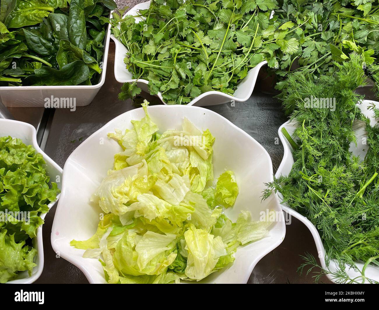 Leckeres und gesundes Essen. Frische grüne Zwiebeln, Petersilie, Dill, Salat, Spinat in weißen Schalen werden zum Buffet serviert. Stockfoto