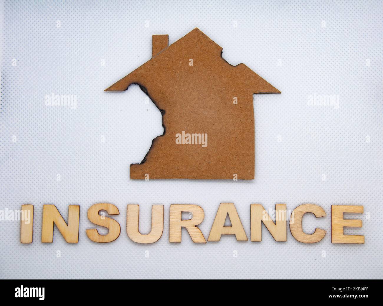 Versicherung Holztext mit verbranntem Modellhaus auf weißem Hintergrund. Versicherungskonzept. Stockfoto