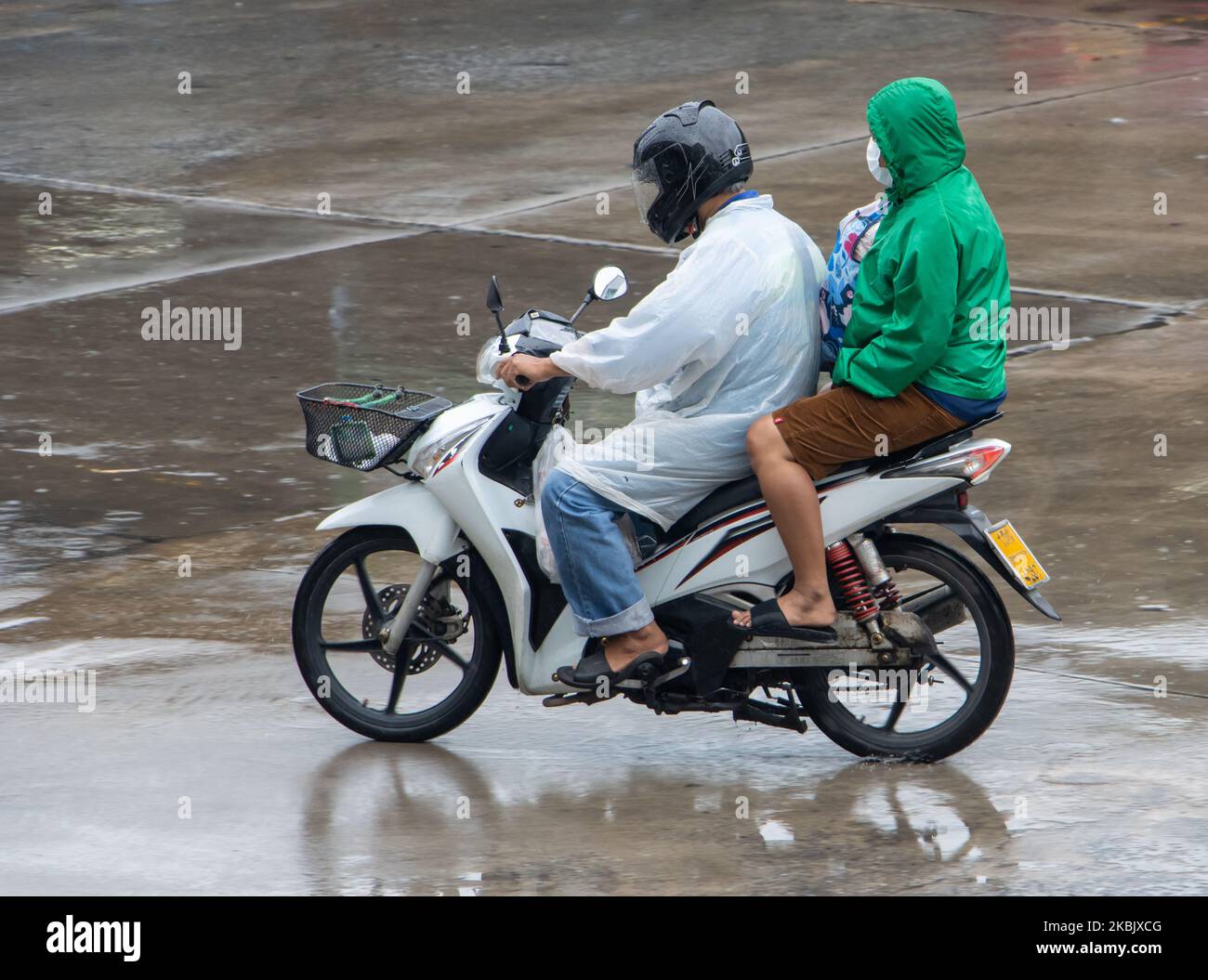 Ein Paar im Regenmantel fährt auf nasser Straße mit dem Motorrad Stockfoto