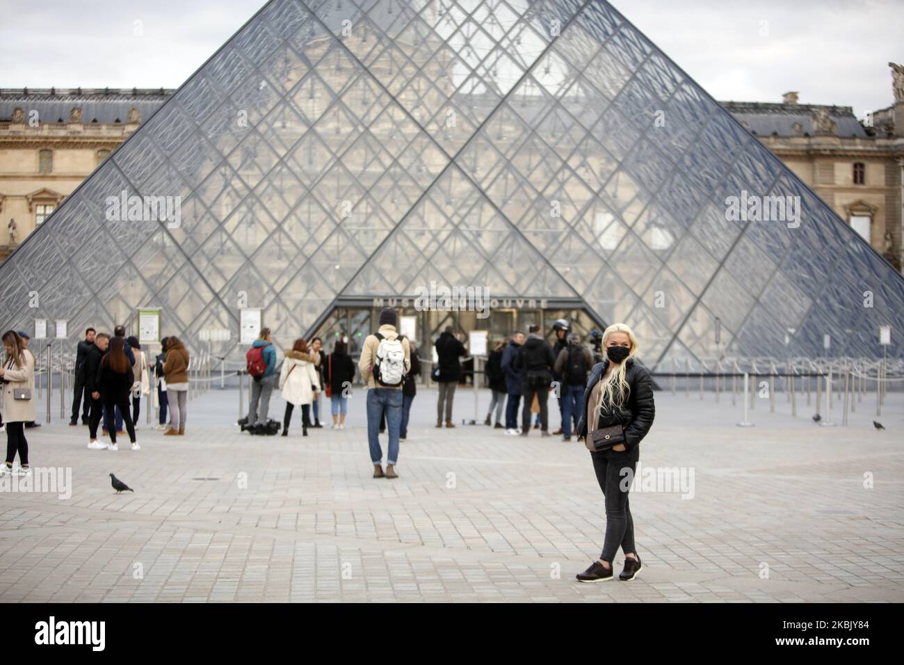 Touristen mit Schutzmasken gehen vor dem Pariser Musée du Louvre, das aufgrund der Besorgnis über den COVID-19-Ausbruch, der durch das neuartige Coronavirus verursacht wurde, am 13. März 2020 für die Öffentlichkeit auf unbestimmte Zeit gesperrt ist. Der Louvre in Paris, das am meisten besuchte Museum der Welt, sagte am 13. März 2020, dass es wegen des Coronavirus „bis auf weiteres“ geschlossen würde. Die Schließung des Museums, das letztes Jahr 9,6 Millionen Besucher hatte, erfolgte, nachdem die französische Regierung alle Versammlungen von über 100 Personen verboten hatte, um die Ausbreitung des Virus zu begrenzen. Das Schloss von Versailles -- Frankreichs andere große Touristenattraktion Stockfoto