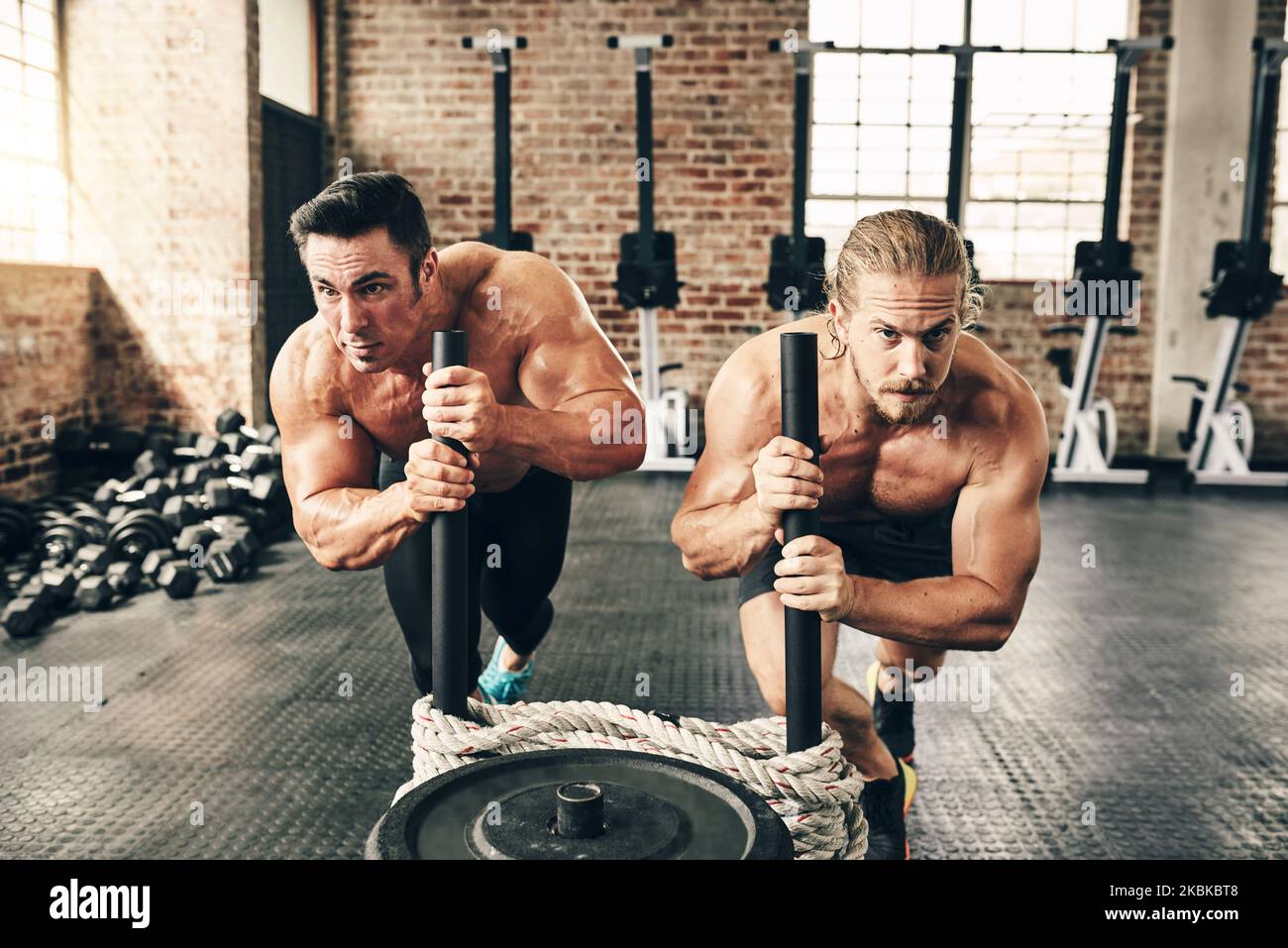 Keine Anstrengung. Zwei fitte und entschlossene junge Männer, die mit Gewichten gemeinsam in einem Fitnessstudio trainieren. Stockfoto