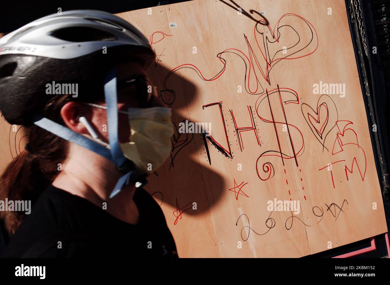 Eine Frau, die eine Maskenrolle trägt, läuft an einer Liebesbotschaft für den National Health Service (NHS) vorbei, die am 4. April 2020 auf die Holzlaken eines aufgeketteten Restaurants in der New Oxford Street in London, England, geschrieben wurde. In ganz Großbritannien wurden bisher insgesamt 41.903 Fälle des Covid-19-Coronavirus bestätigt, wobei 4.313 Menschen starben. Das Land befindet sich mittlerweile fast zwei Wochen in seiner „Sperre“, die nach einer ersten dreiwöchigen Frist überprüft werden soll, obwohl eine Verlängerung weithin erwartet wird. Der britische Staatssekretär für Gesundheit und Soziales, Matt Hancock, bestand darauf Stockfoto