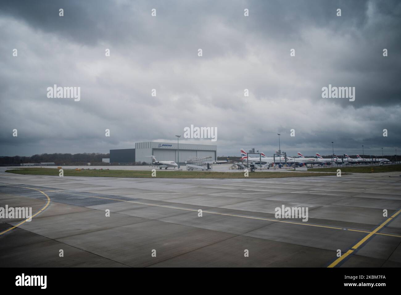 British Airways-Jets Reihen sich mit einem Privatjet im Vordergrund, Ladungshallen im Hintergrund bei schlechtem Wetter Taxibereich vor Stockfoto