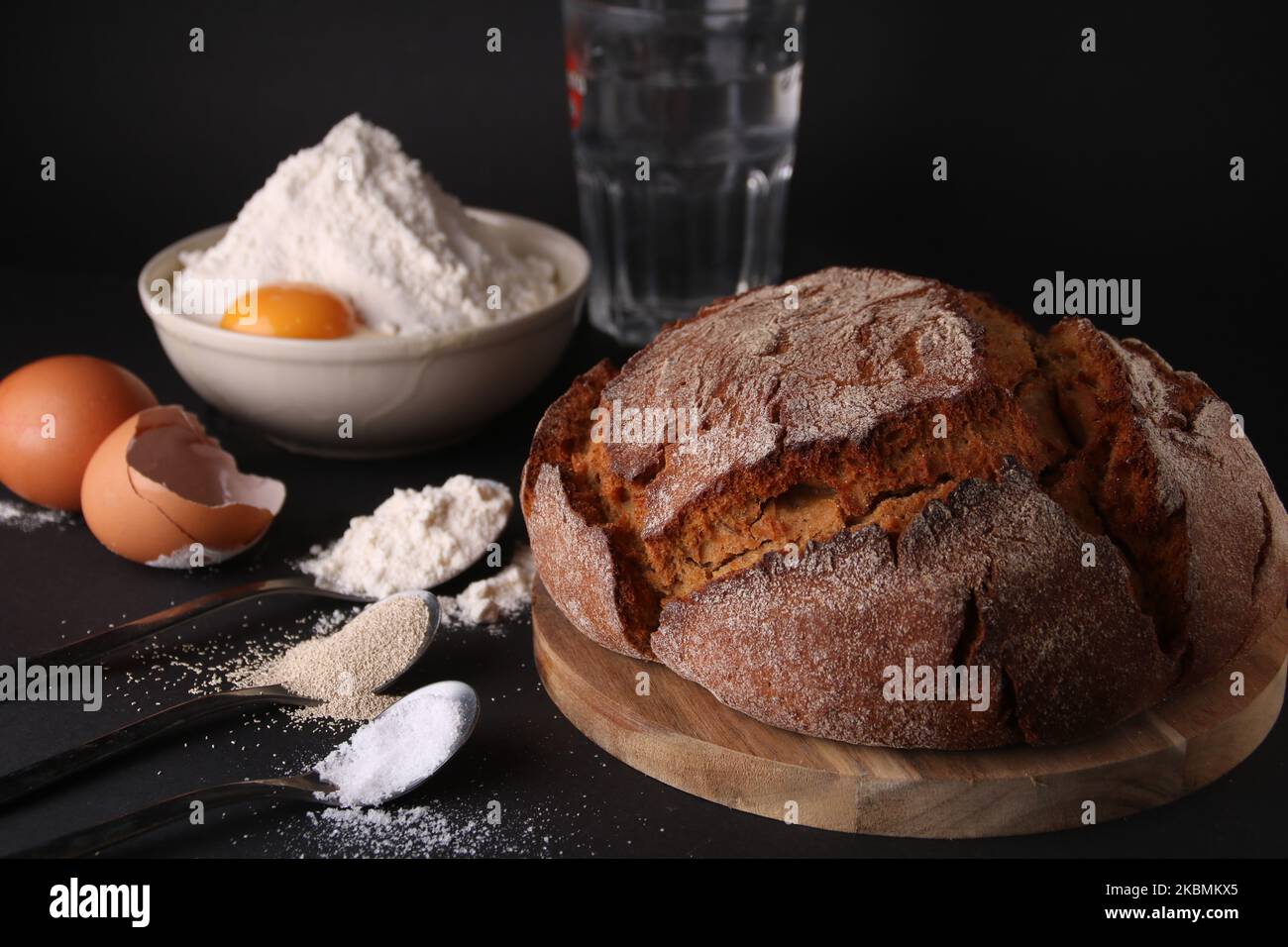 Frisches, rundes Brot auf dem Brett neben den Zutaten für die Zubereitung Stockfoto