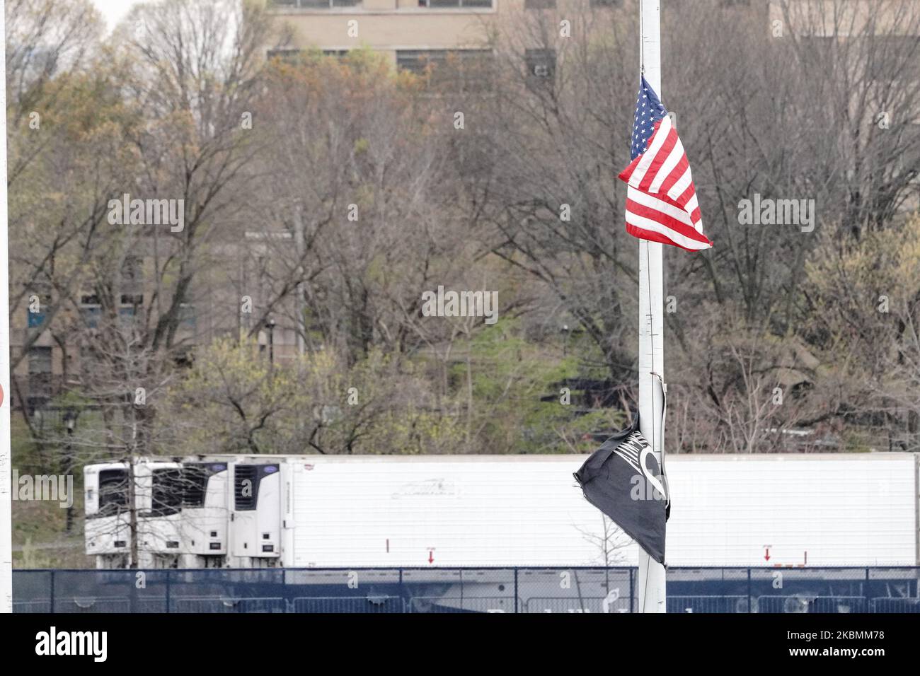 Eine Ansicht der amerikanischen Flagge auf der Hälfte des Personals vor Reihen von gekühlten Leichenhallen in einem Depot im Randall’s Island Park, New York City, USA während der Coronavirus-Pandemie am 19. April 2020. (Foto von John Nacion/NurPhoto) Stockfoto