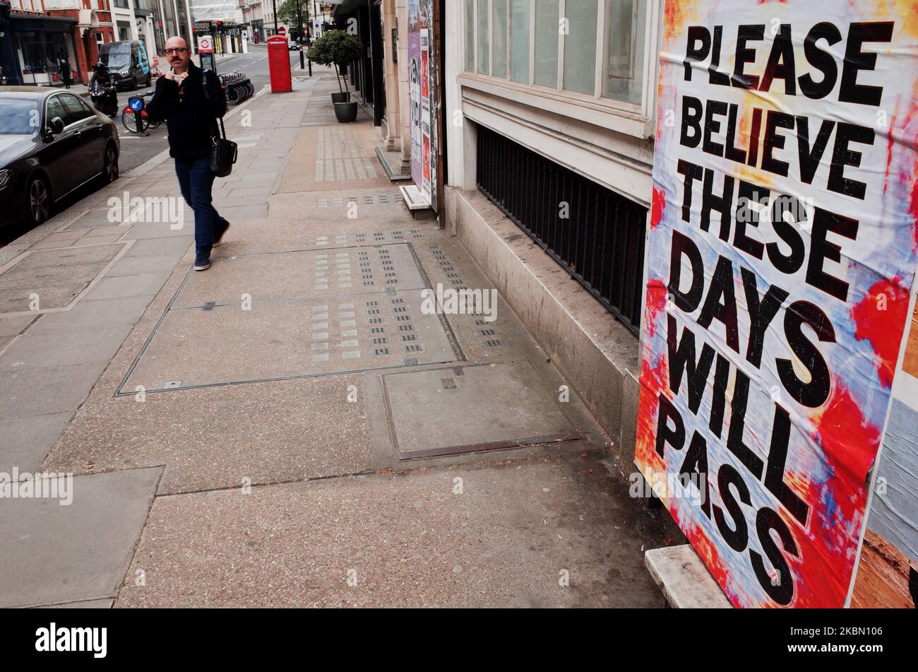 Ein Mann geht am 27. April 2020 in der Bruton Street im Londoner Stadtteil Mayfair in England an ein Plakat mit der Botschaft der Hoffnung „Please Believe These Days will Pass“ des Künstlers Mark Titchner heran. Großbritannien begann heute mit der sechsten Woche der Blockierung des Coronavirus, und Premierminister Boris Johnson forderte das Land heute Morgen auf, sich mit den Maßnahmen weiter zu gedulden, während das Vereinigte Königreich seinen „Höhepunkt“ von 19 kovidbedingten Fällen und Todesfällen übersteht. In den letzten Wochen wurde der Ruf nach der Regierung laut, ihre Überlegungen darüber anzustellen, wann und wie das Land beginnen könnte, einige der derzeit geltenden Beschränkungen zu vergießen Stockfoto