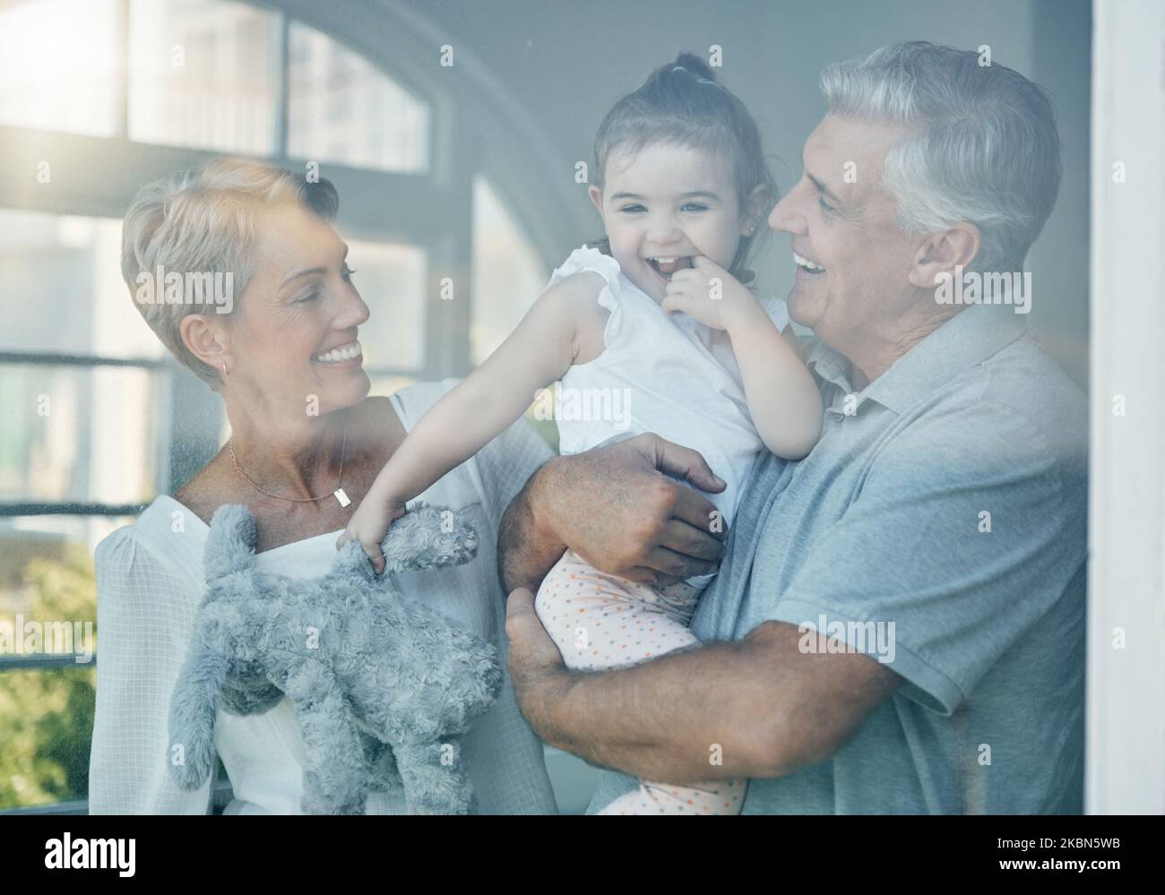 Familie, Glück und Liebe der Großeltern für das Baby im Fenster zu Hause zum Kleben, entspannen und genießen Sie Zeit zusammen. Ältere Männer und Frauen, die Spaß und Fürsorge haben Stockfoto