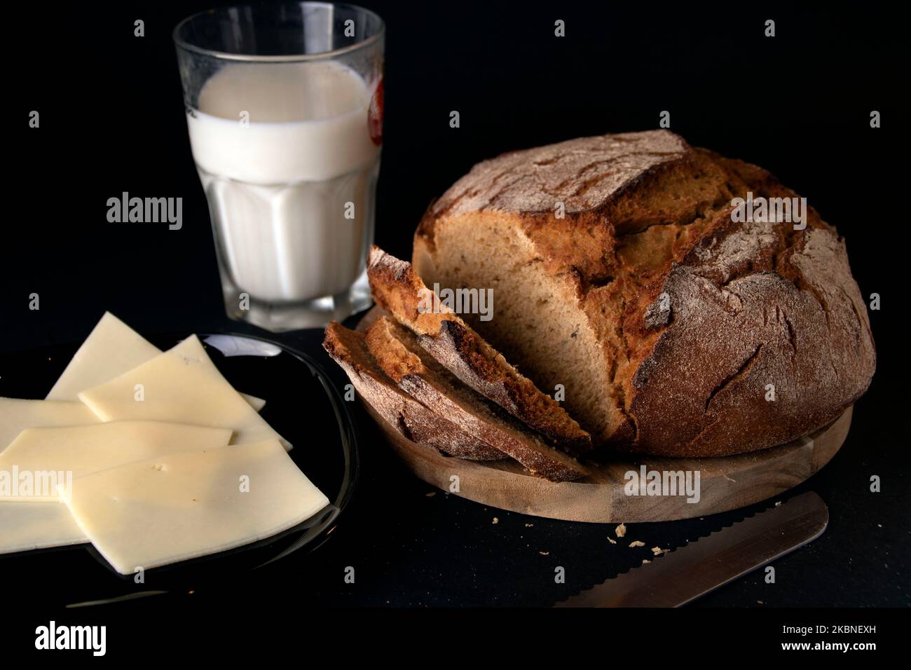 Foto von frisch geschnittenem Brot auf einem hölzernen Küchbrett mit einem Glas Milch und Käse Stockfoto