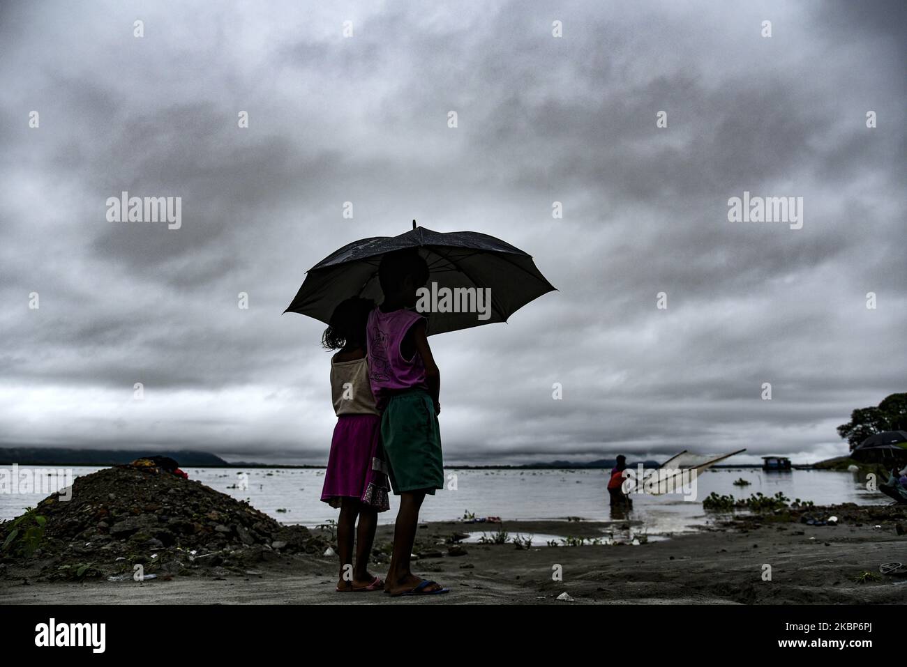 Kinder unter einem Regenschirm am Ufer des Flusses Brahmaputra vor dem Hintergrund dunkler Wolken, die den Himmel an einem regnerischen Tag bedecken, am Samstag, den 23. Mai in Guwahati, Assam, Indien, 2020. (Foto von David Talukdar/NurPhoto) Stockfoto