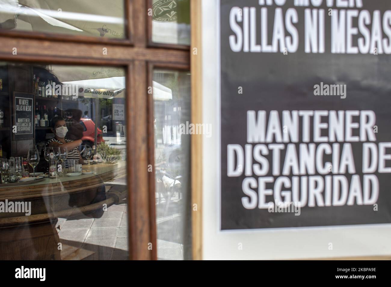 Eine Kellnerin durch das Fenster ihrer Cafeteria am ersten Tag der Eröffnung nach mehr als zwei Monaten inaktiv. Das Außenschild warnt vor dem Verbot, „Stühle und Tische zu bewegen“ und erinnert daran, „den Sicherheitsabstand zu halten“. In Norena, Asturien, Spanien, am 25. Mai 2020. Mehrere spanische Regionen beginnen an diesem Montag die Phase 2 der zwei Wochen andauenden Deeskalation, die Isolationsmaßnahmen flexibler macht, aber soziale Distanzierungen priorisiert, um die Ausbreitung von Covid-19 zu verhindern. Bars und Restaurants beginnen, Essen in ihren Räumlichkeiten zu servieren, mit einem Maximum von 40% der Kapazität und Aufrechterhaltung 2 mete Stockfoto