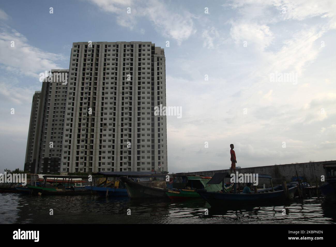 Der Junge steht auf dem traditionellen Fischerboot gegen Unterbau-Wohnungstürme, während sein Vater am 3. Juni 2020 inmitten der Coronavirus-Pandemie Covid-19 am alten Hafen von Sunda Kelapa in Nord-Jakarta das Fischernetz repariert. (Foto von Aditya Irawan/NurPhoto) Stockfoto