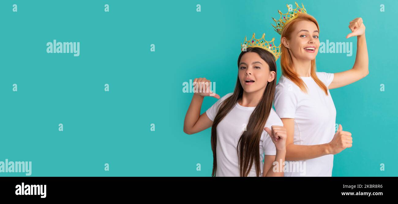 Mutter-Tochter-Kinderbanner, Kopierraum, isolierter Hintergrund. Glückliche Frau und Mädchen Kind in Kronen zeigen Finger auf Werbe-T-Shirts für Kopie Stockfoto