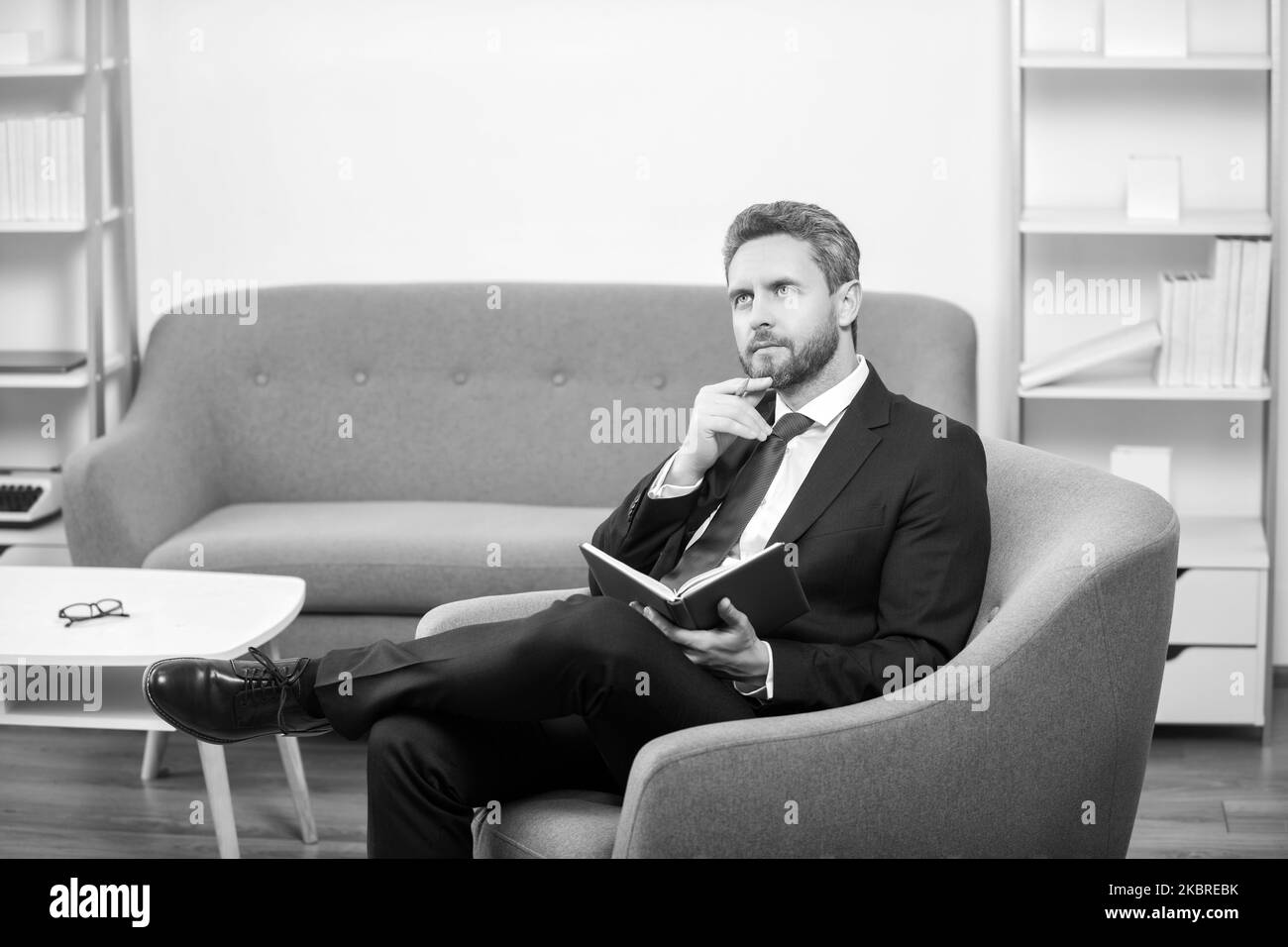 Reifer Geschäftsmann im Anzug sitzen im Lesebüro und machen sich Notizen im Notizbuch Stockfoto