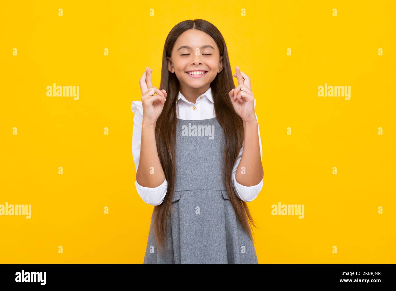 Teenager Kind Mädchen, die ihre Finger kreuzt und viel Glück wünscht, isoliert auf gelbem Studiohintergrund mit Kopierraum. Stockfoto