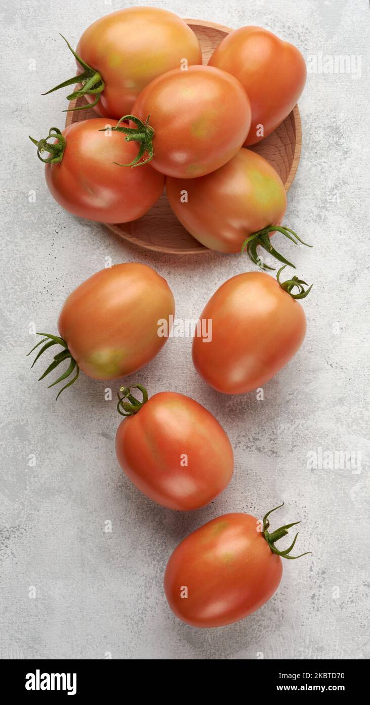 Reife Tomaten auf einem Holzteller mit verstreuter weißer Strukturoberfläche, essbare Beeren von oben Stockfoto