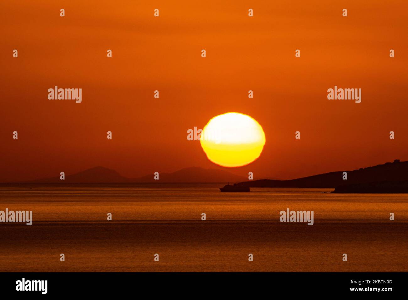 Verträumter Sonnenuntergang während der goldenen Stunde vor der Dämmerung mit dem Himmel in Rot, Orange und warmen Farben, wenn die Sonne hinter der Ägäis über Mykonos Stadt oder Chora, auf Myconos Insel in den Kykladen, Ägäis in Griechenland untergeht. Die berühmte griechische Mittelmeerinsel wird mit weiß getünchten traditionellen Gebäuden wie Windmühlen oder einer kleinen Kirche als Insel der Winde bezeichnet. Mykonos ist eine beliebte Insel für Prominente und Touristen, die im pulsierenden Nachtleben feiern möchten. Die Insel gilt auch als homosexuell freundlich. Die griechische Regierung hat die Sommersaison durch eine Lockerung der verkehrsberuhigten Straßen wieder aufgenommen Stockfoto