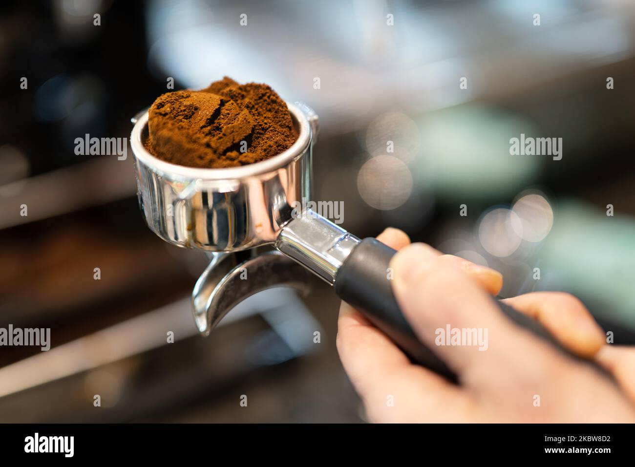 Eine Hand, die einen Portafilter mit frisch gemahlenem Kaffee hält, stapelt sich in Live-Atmosphäre. Stockfoto