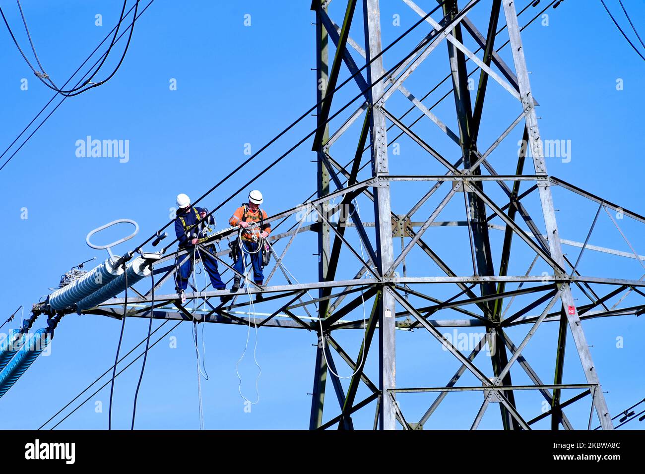 Elektrisch angepylonierte Arbeiter hoch über dem Boden reparieren Kabel gegen klaren blauen Himmel Stockfoto