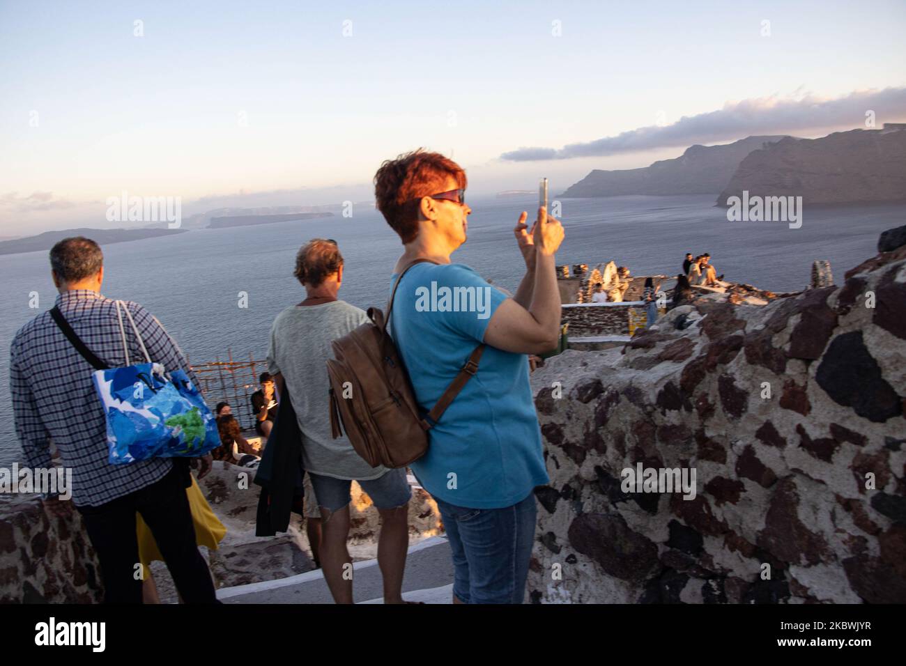 Touristen genießen den atemberaubenden Sonnenuntergang in Oia auf der Insel Santorini, auf den Kykladen, der Ägäis, in Griechenland. Sie befinden sich an einem Aussichtspunkt auf der alten traditionellen Burg und den Dächern von Häusern, Kirchen und Hotels, die auf den vulkanischen Klippen errichtet wurden. Touristen aus der ganzen Welt sind entspannt und fotografieren und Selfies mit Handys und Kameras die Sonne geht im Mittelmeer unter. Die Insel ist berühmt für den magischen Sonnenuntergang, die Architektur der weiß getünchten Häuser, Hotels mit Blick auf den Pool und die blauen Kuppelkirchen am steilen Rand der Klippe. Santorini ist ein beliebtes Ziel für Flitterwochen Stockfoto