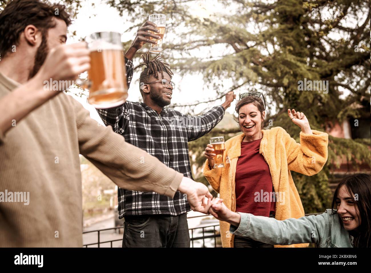 Fröhliche Gruppe verschiedener multiethnischer junger Freunde, die Bier trinken und gemeinsam auf einer Tanzparty im Freien Spaß haben - vielrassige, schwungige Menschen feiern Stockfoto