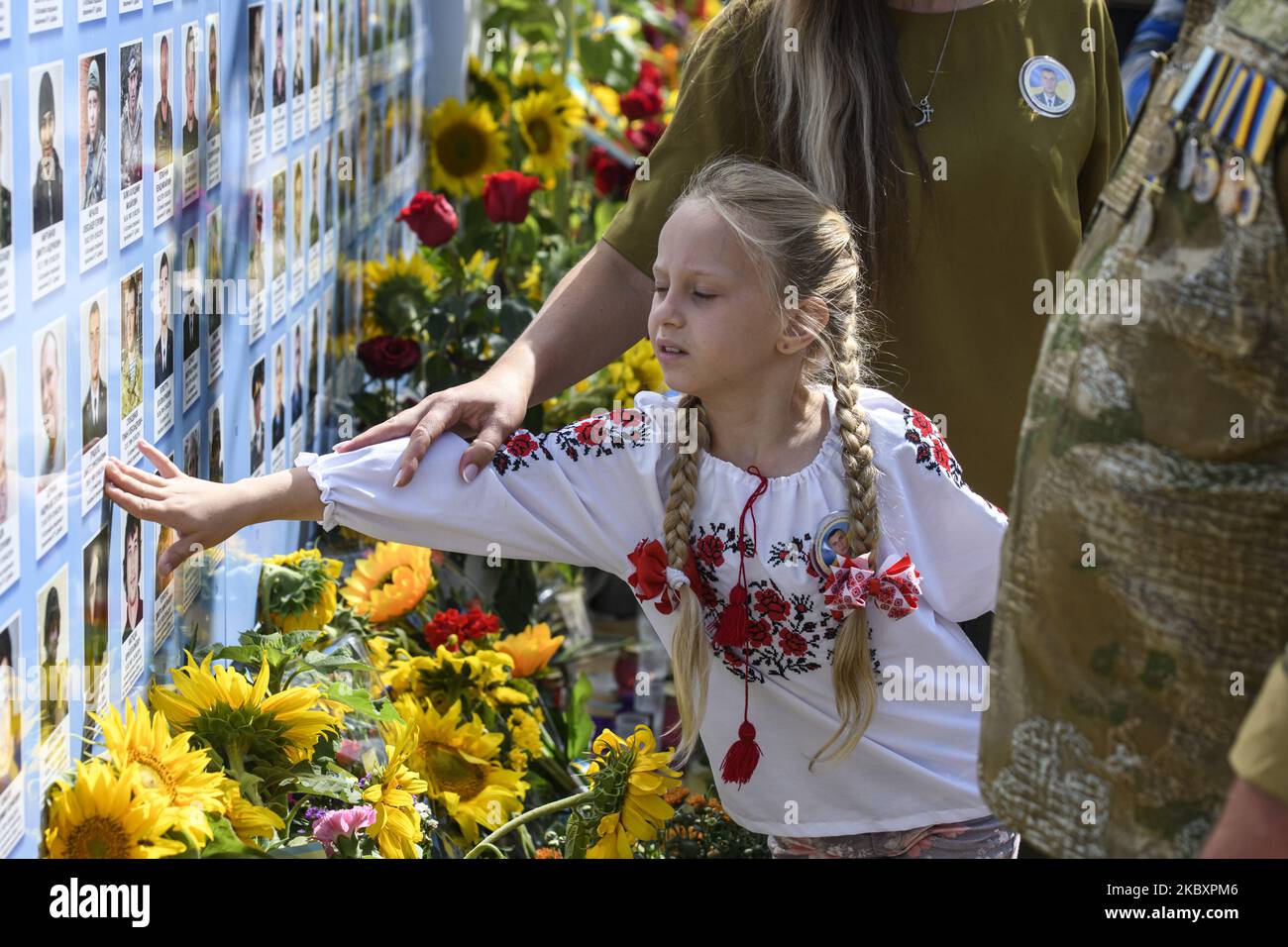 Ein Mädchen berührt ein Porträt über die Gedenkmauer der gefallenen Verteidiger der Ukraine im Krieg in der Ostukraine 2014-2020 während einer Gedenkfeier zum Gedenktag der gefallenen Verteidiger der Ukraine in Kiew, Ukraine, 29. August 2020. (Foto von Maxym Marusenko/NurPhoto) Stockfoto