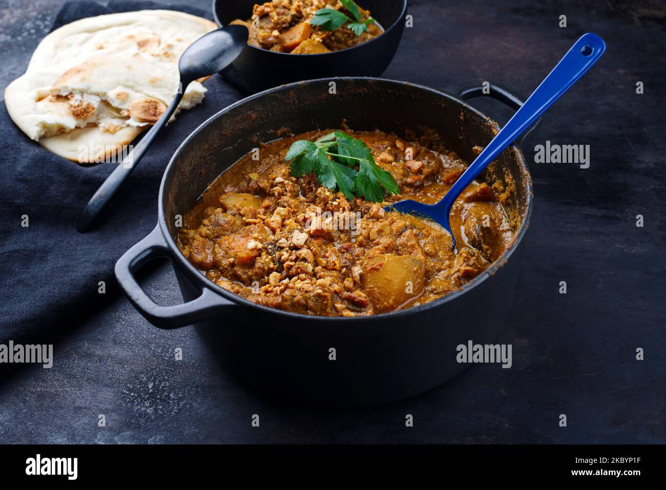 Traditioneller indischer vegetarischer Madras-Eintopf mit Süßkartoffeln, gerösteten Cashewnüssen und Knoblauchkapati-Brot aus nächster Nähe in Kochtöpfen Stockfoto